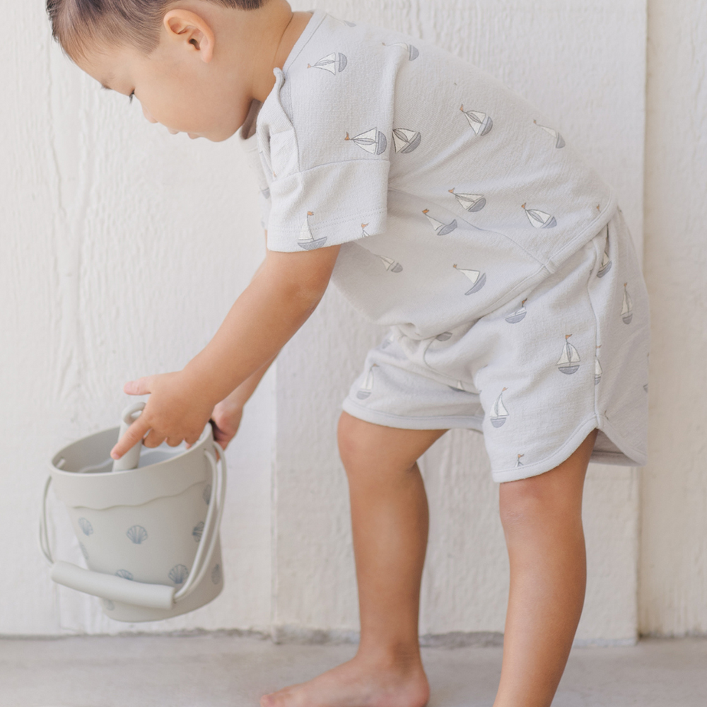 
                      
                        A playful moment of a toddler boy filling his beach bucket while wearing the Quincy Mae Spongy Play Set, a must-have outfit for spring break and summer fun.
                      
                    