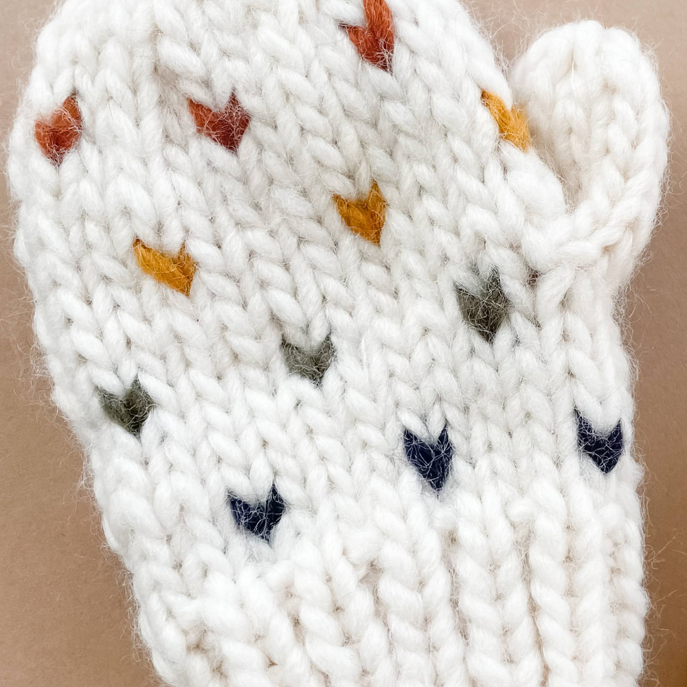 A detailed close-up view of the Sawyer Heart Mittens by Blueberry Hill, showcasing the soft hand-knit texture and charming heart design in pastel hues.