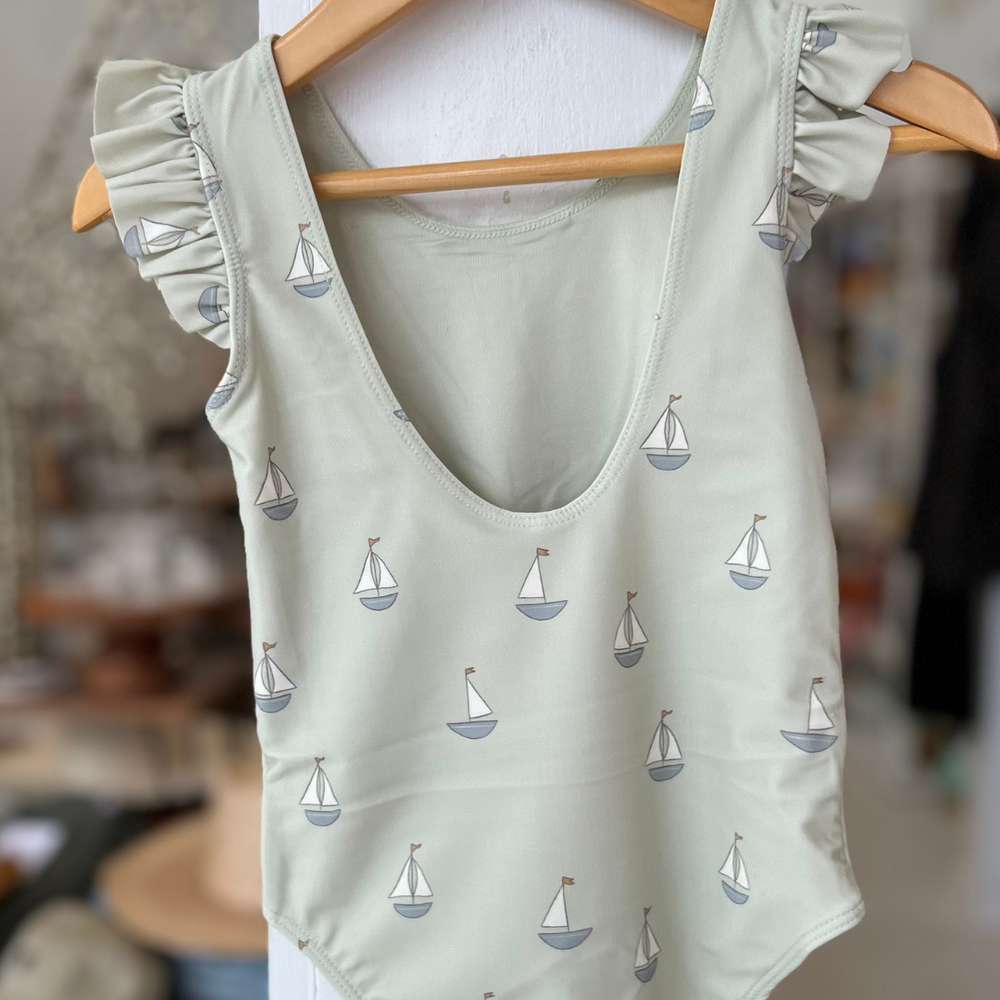 
                      
                        Featuring a delicate sailboat print on a soft, muted green background, this swimsuit brings a classic coastal vibe to beach days and poolside fun.
                      
                    