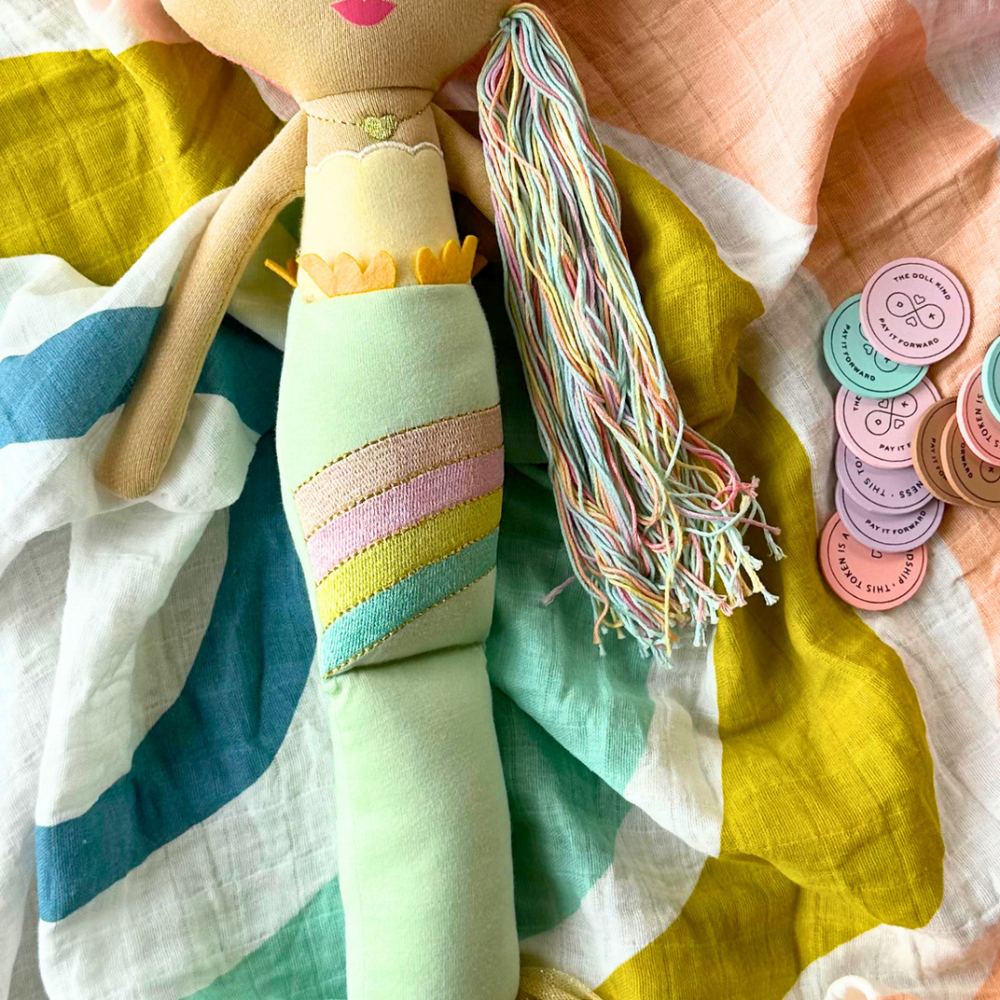 Beautiful arrangement featuring the enchanting Shine Mermaid Kindness Doll with kindness tokens, perfect for inspiring generosity and love, placed on a soft, colorful muslin swaddle.