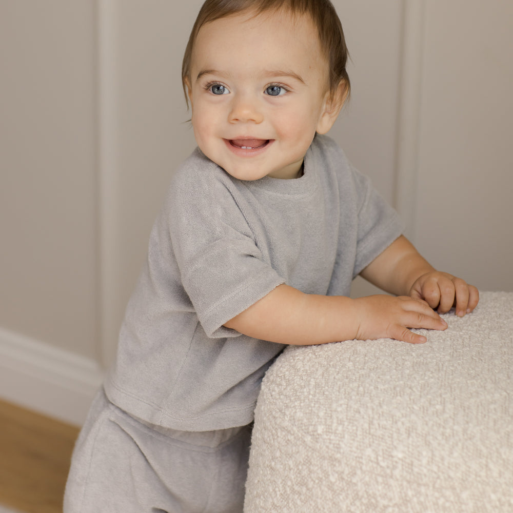 Adorable toddler boy wearing the Quincy Mae Organic Cort Terry Matching Top & Shorts set. The soft and cozy organic cotton fabric ensures comfort all day long, while the stylish terry design adds a modern touch. Perfect for warm weather, this set combines playful style with sustainability, making it a great choice for active little ones. The matching top and shorts offer a coordinated look, ideal for any occasion.