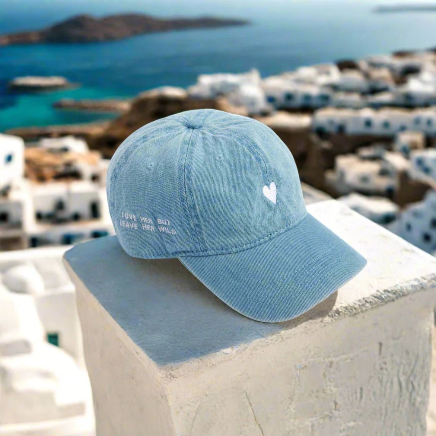 Blue denim cap with a heart design on a ledge with a scenic background of a coastal town.