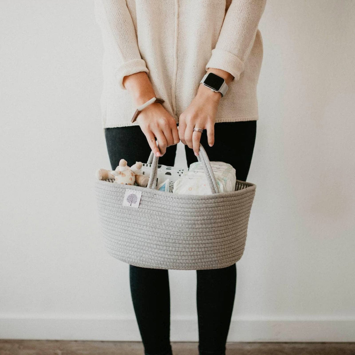 Woman holding a baby tote fully of diapers, Raz Baby pacifiers, and more baby essentials. 
