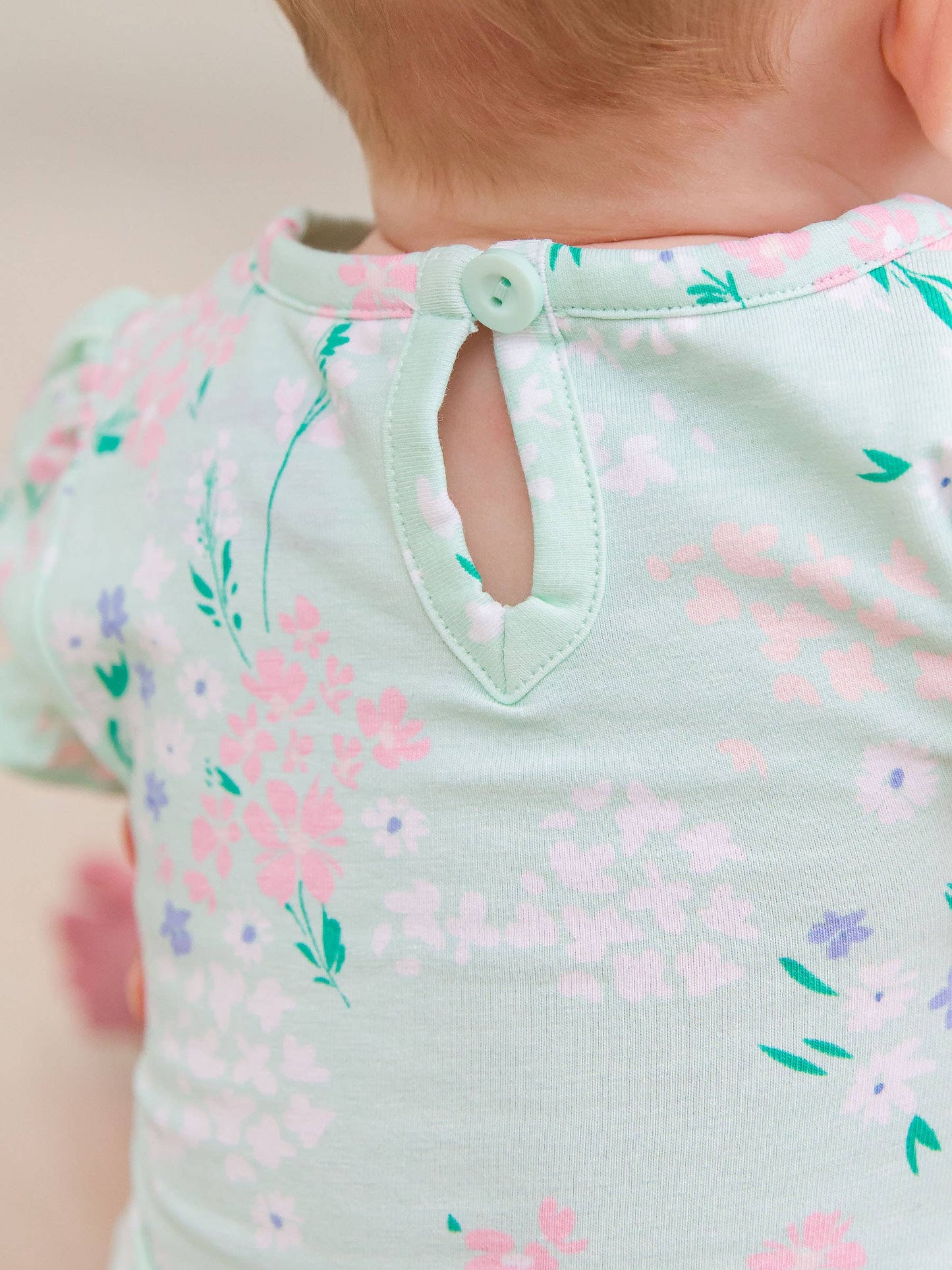 Close-up of back detail on baby girls mint meadow bodysuit showing soft fabric and stitching near snap closures