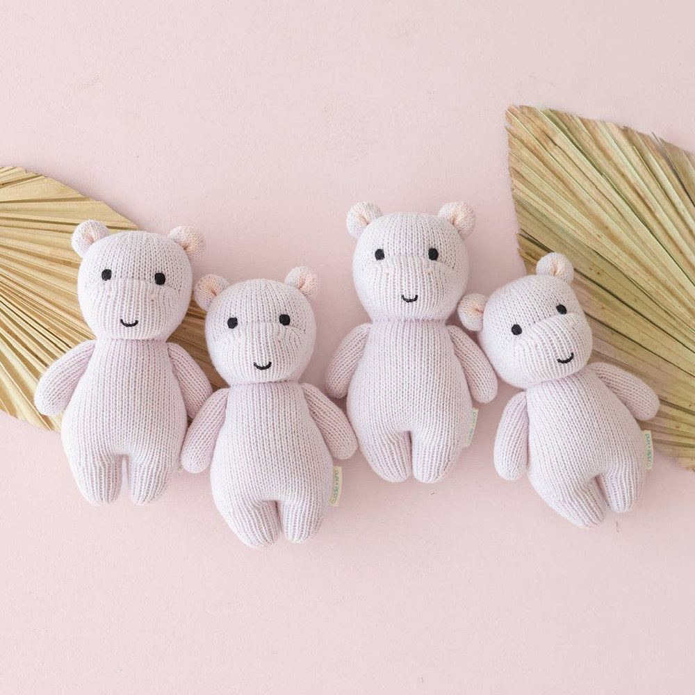 
                      
                        Four lavender baby hippo dolls lined up side by side, showcasing consistency in handmade fair trade craftsmanship
                      
                    