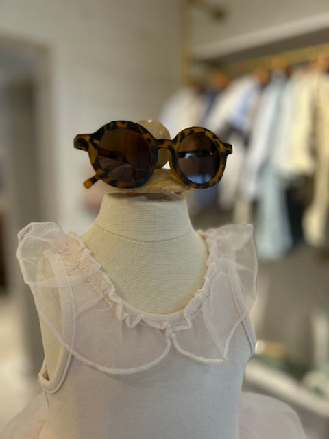Baby wearing stylish round sunglasses with frilly dress for sun protection and spring wedding style, also perfect for Easter.