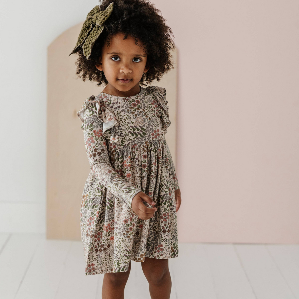 
                      
                        Full view of little girl wearing the adorable Winter Floral ruffle dress, ideal for special occasions or everyday wear, combining style and comfort.
                      
                    