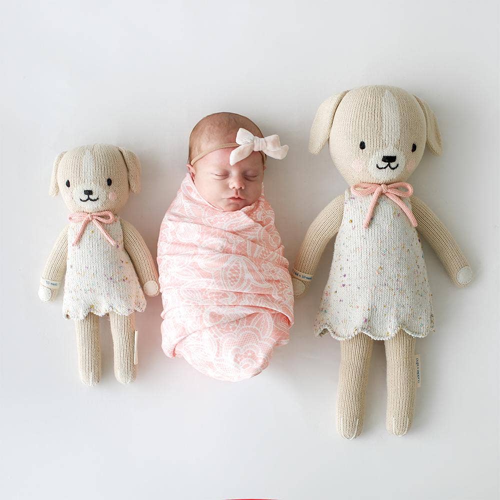 
                      
                        Smiling baby lying down with Mia the Dog dolls in both sizes on each side
                      
                    