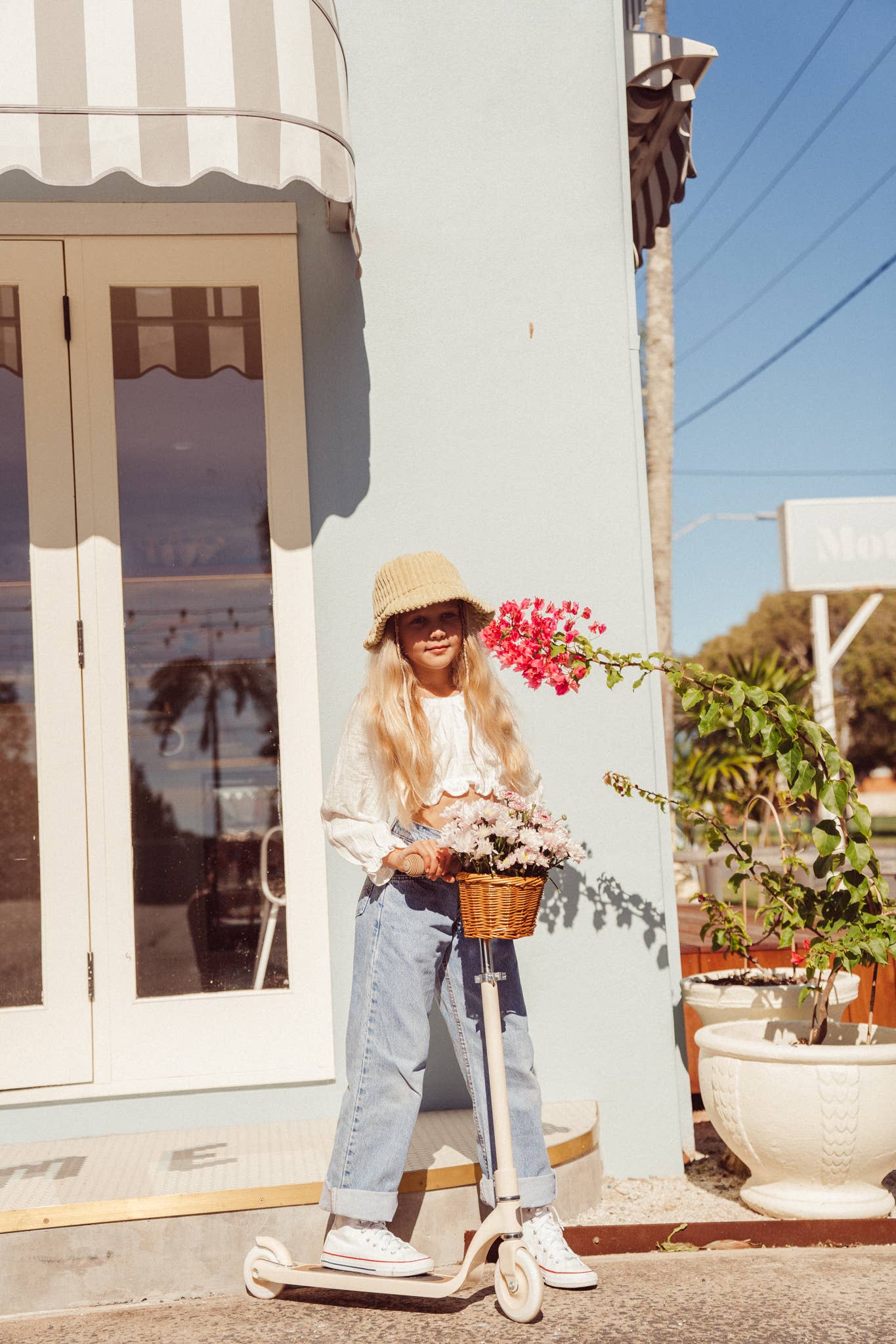 Child riding Banwood Maxi Scooter Vintage in Cream — two-wheel aluminum scooter with oak deck and wicker basket, outdoor summer setting