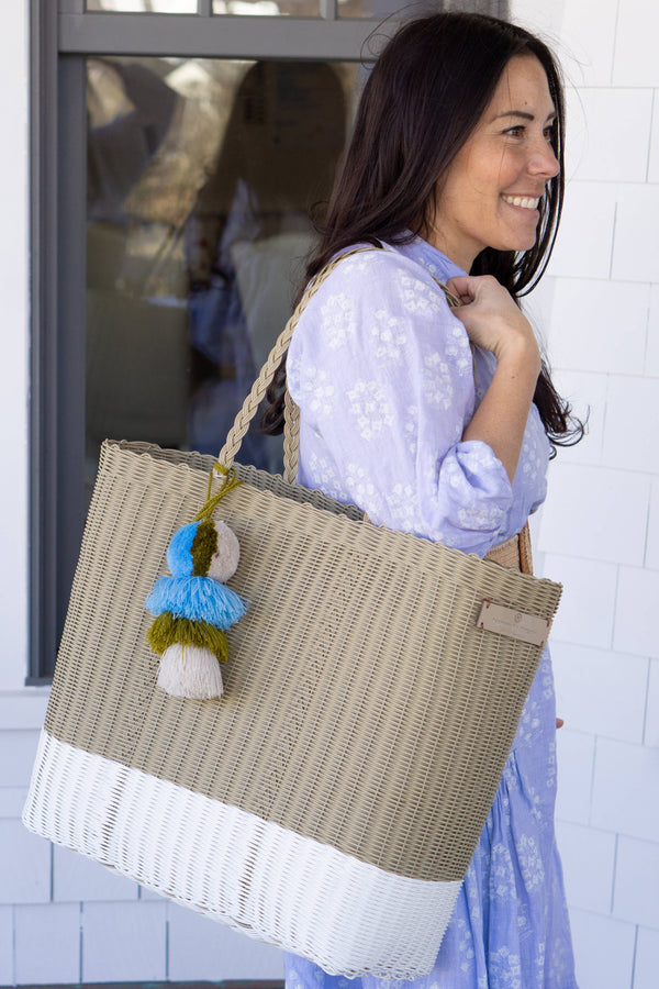 Cafe con Leche Citron Tote featuring a woven straw material with multicolored pom-pom accents, carried by a woman in a light