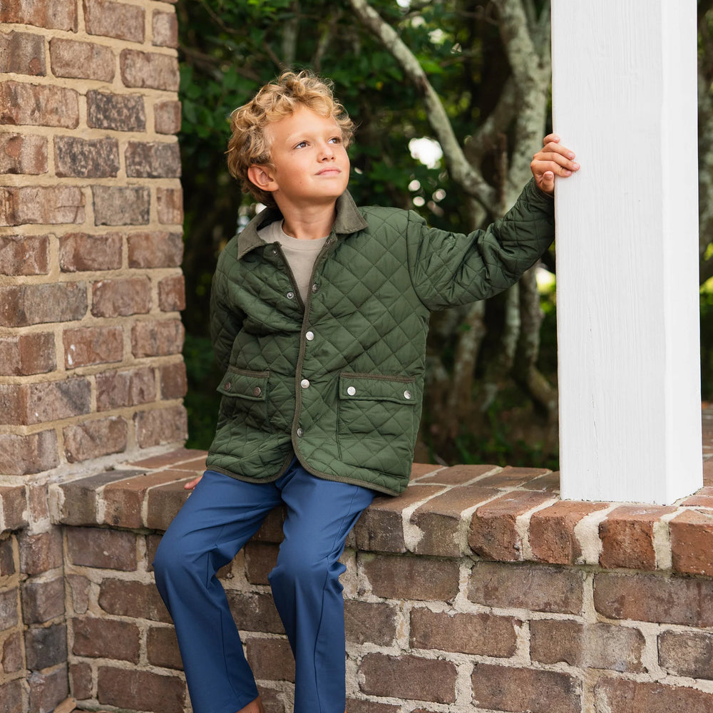 Boy in green Derby Field Jacket sitting on brick wall, highlighting relaxed fit and durable design for everyday play.