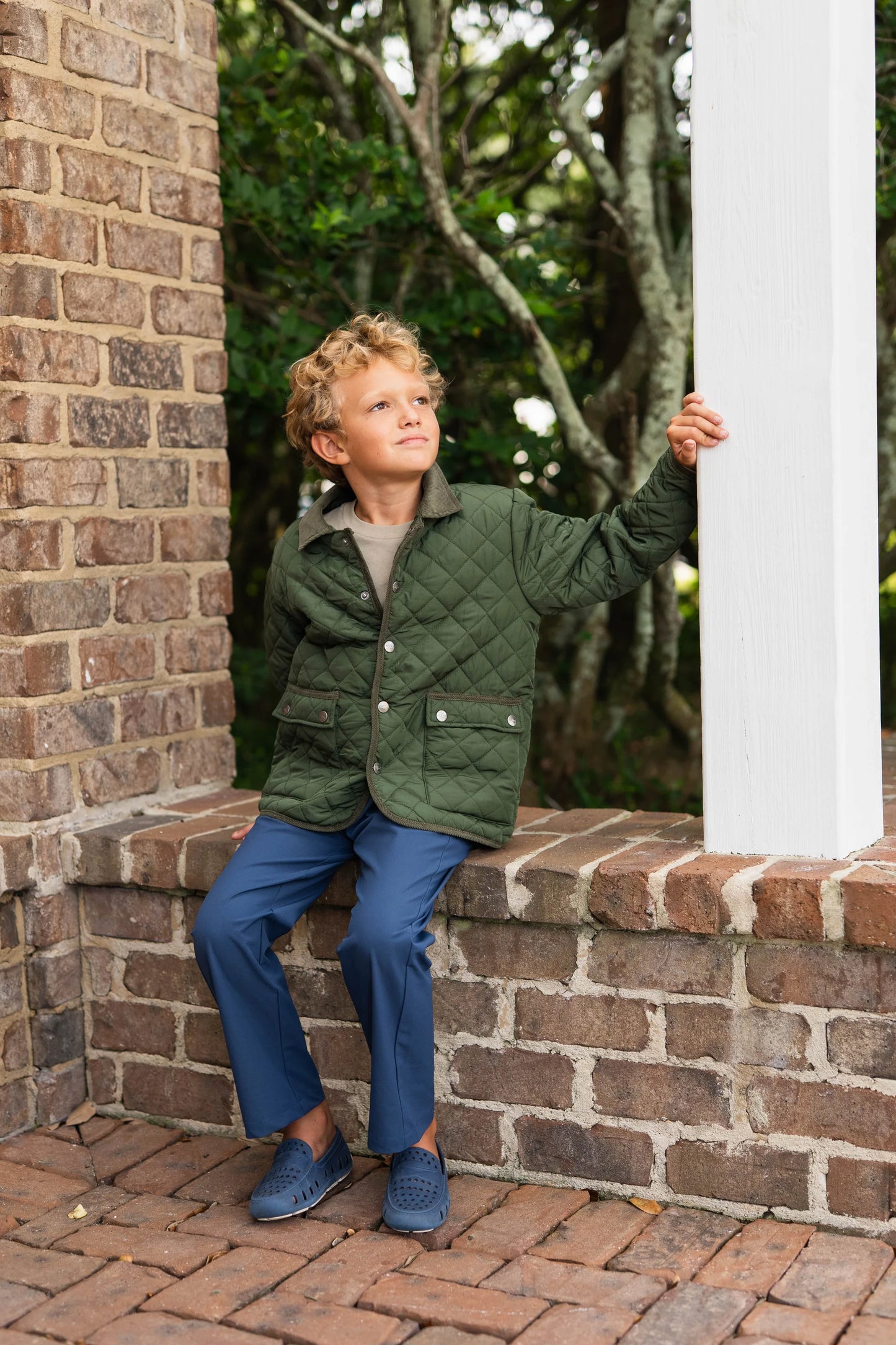Boy in green Derby Field Jacket sitting on brick wall, highlighting relaxed fit and durable design for everyday play.