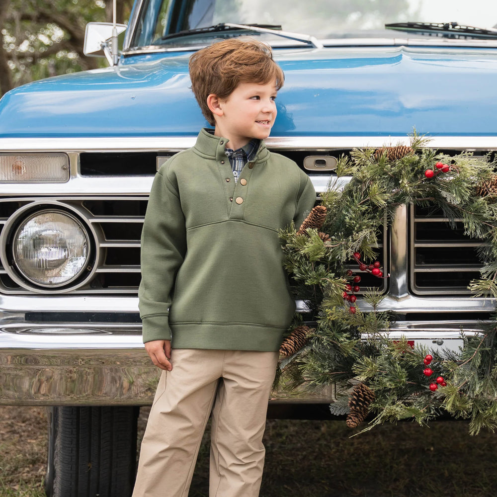 Boy wearing green Pierce Performance Pullover paired with performance pants, standing in front of vintage truck with holiday wreath, showcasing classic fall style.