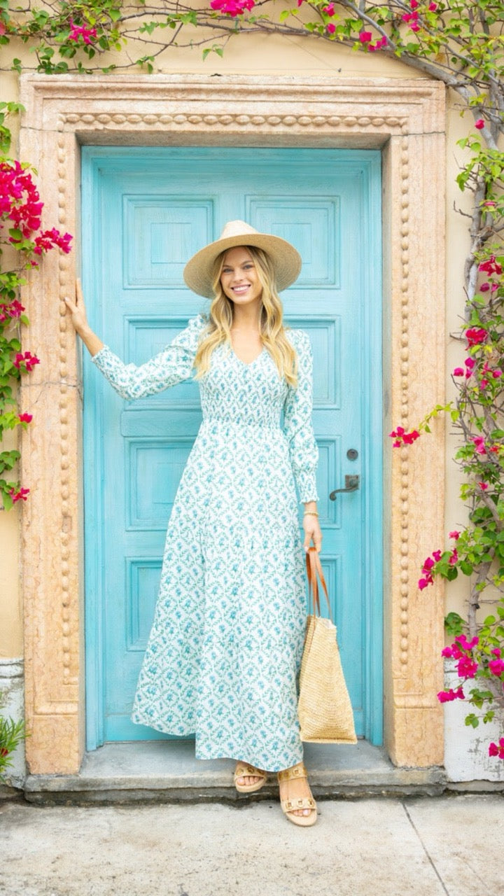 Bridgette Dress in trellis print styled with a straw hat, model standing in front of a coordinating blue door for a resort-ready look.