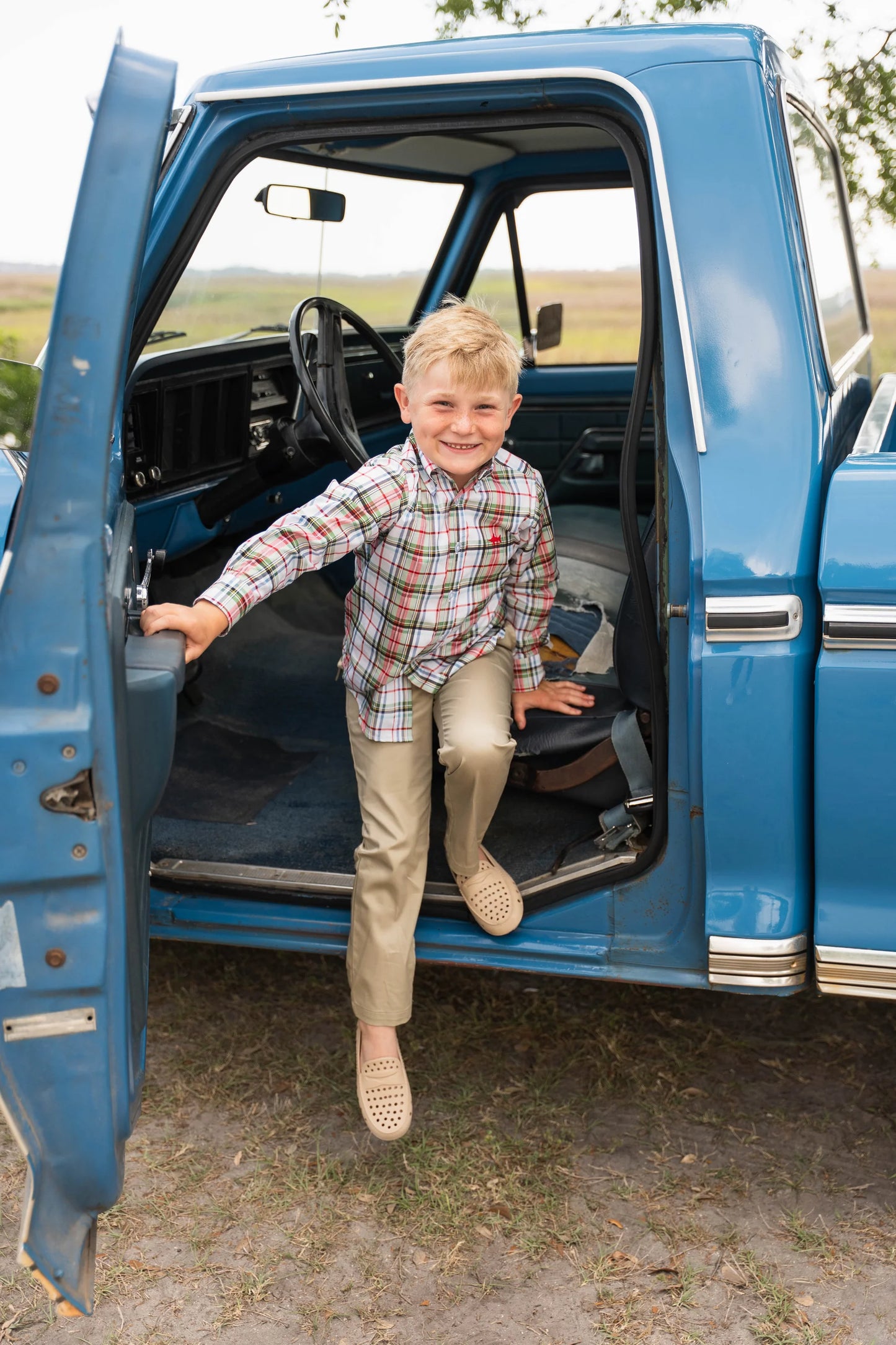 Boy in Carter Oxford Shirt climbing out of old truck, highlighting rugged, playful style and durable design.