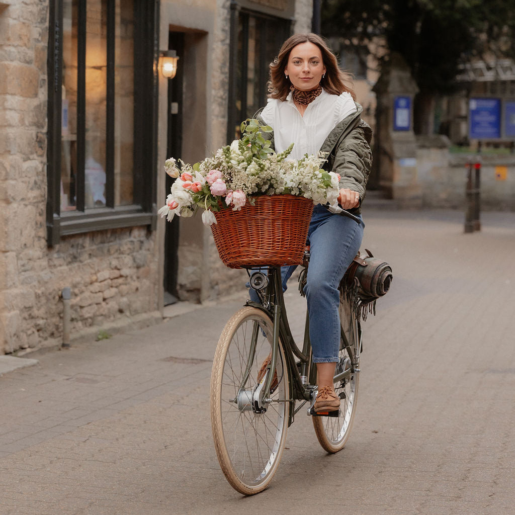 Full outfit lifestyle shot of blouse styled with warm-weather layers riding bicycle with basket of flowers