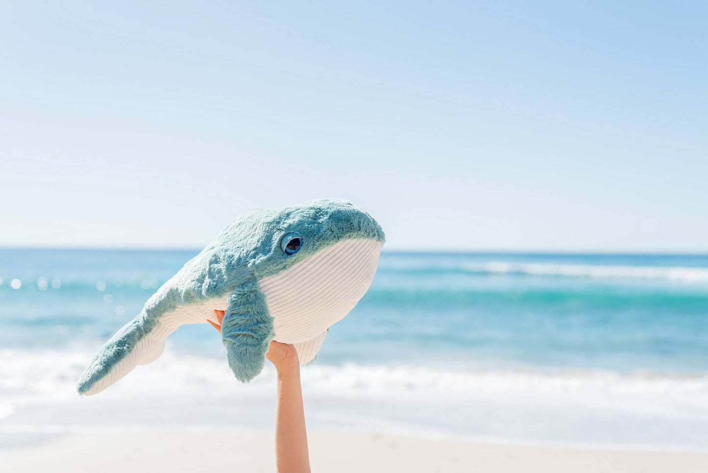 Toddler playing with Hurley Whale plush toy near water, demonstrating imaginative play and soft texture