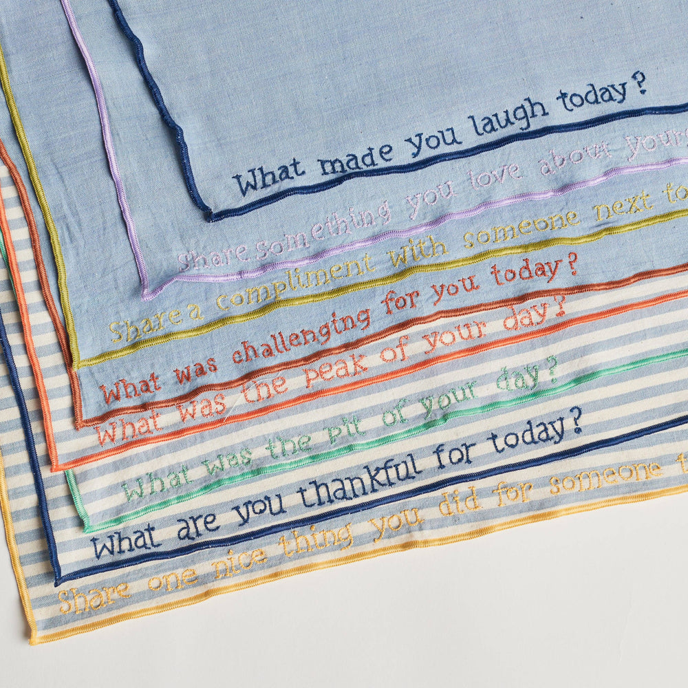 
                      
                        Close-up of a hand-embroidered prompt on one of the conversation napkins, showing fine stitching on chambray fabric
                      
                    