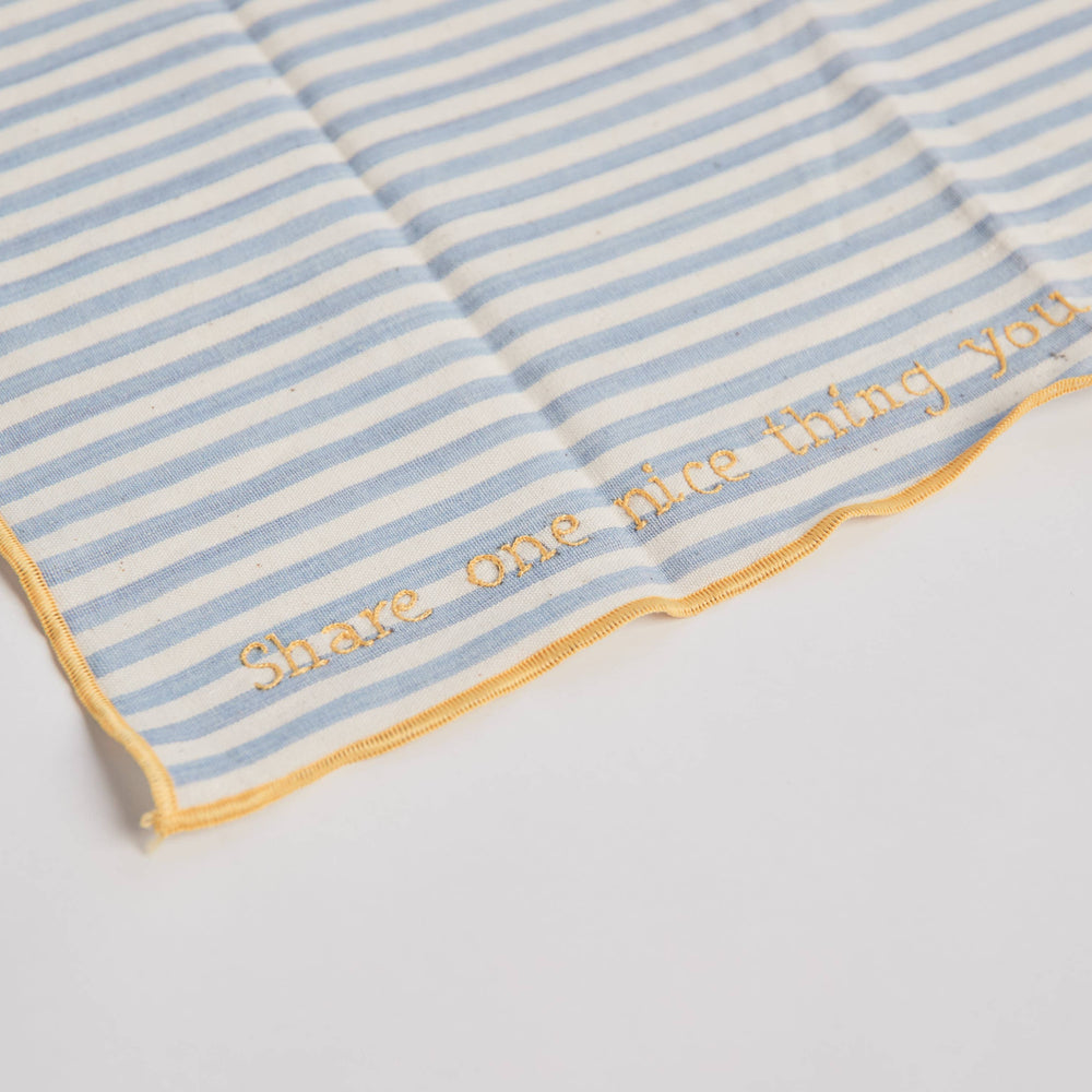 
                      
                        Close-up of a hand-embroidered prompt on one of the conversation napkins, showing fine stitching on chambray fabric
                      
                    