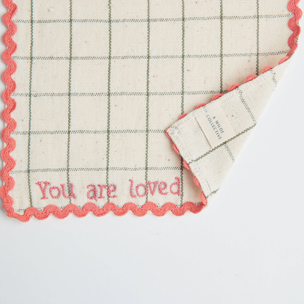 Close-up of the hand-embroidered "You Are Loved" message stitched on a handwoven cotton napkin