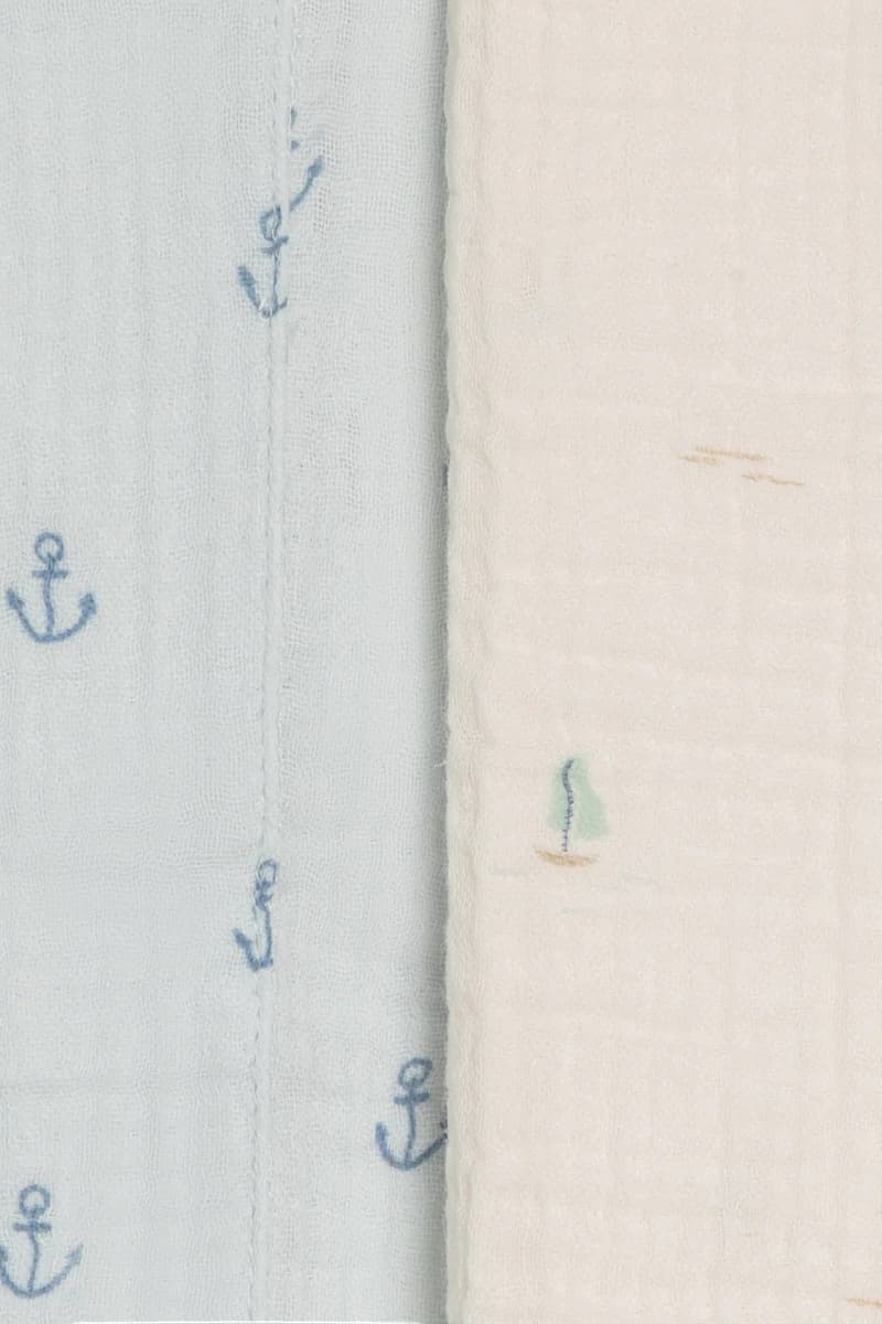 Close-up of Colored Organics Marina sailboat and anchor print muslin burp cloths — muted sailboats on ivory organic cotton and navy anchor motifs on light blue organic cotton