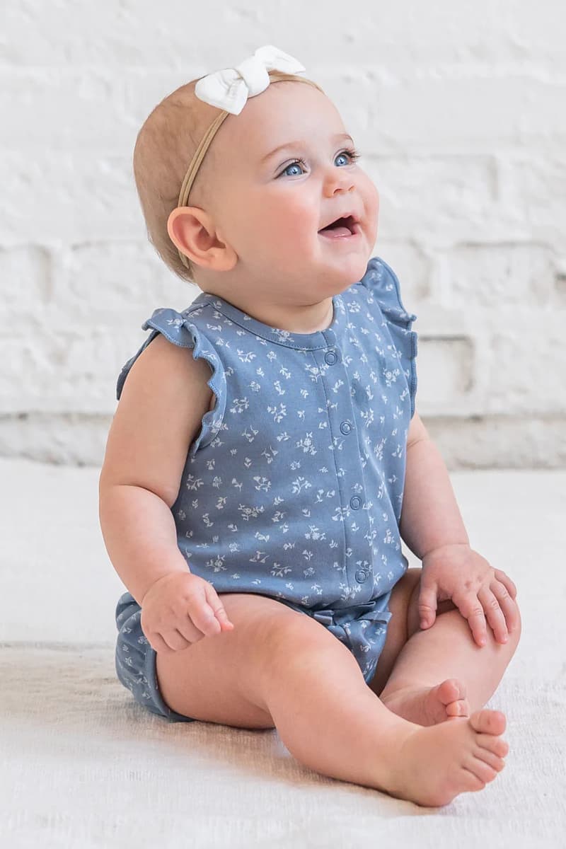 Baby girl wearing Colored Organics Amelia Romper Isla — warm neutral organic cotton with flutter sleeves and cinched waist