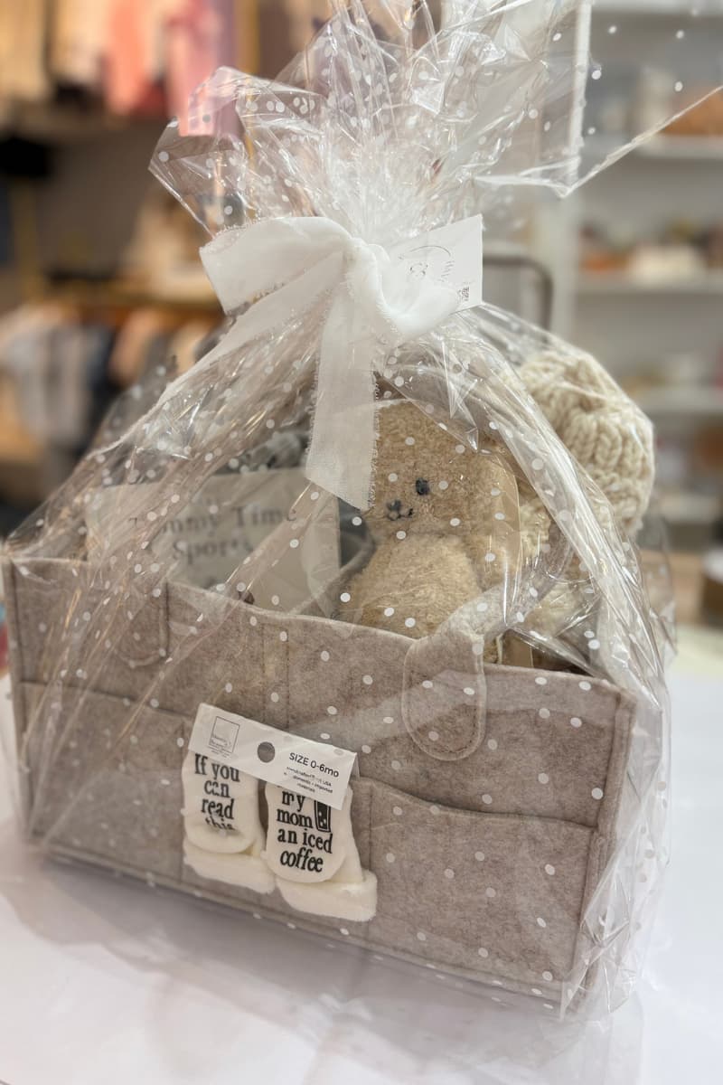 Beautifully wrapped baby shower gift basket full of baby socks, a Cuddle + Kind boucle bear, Tummy Time board book Fisherman Knit baby sweater and more!