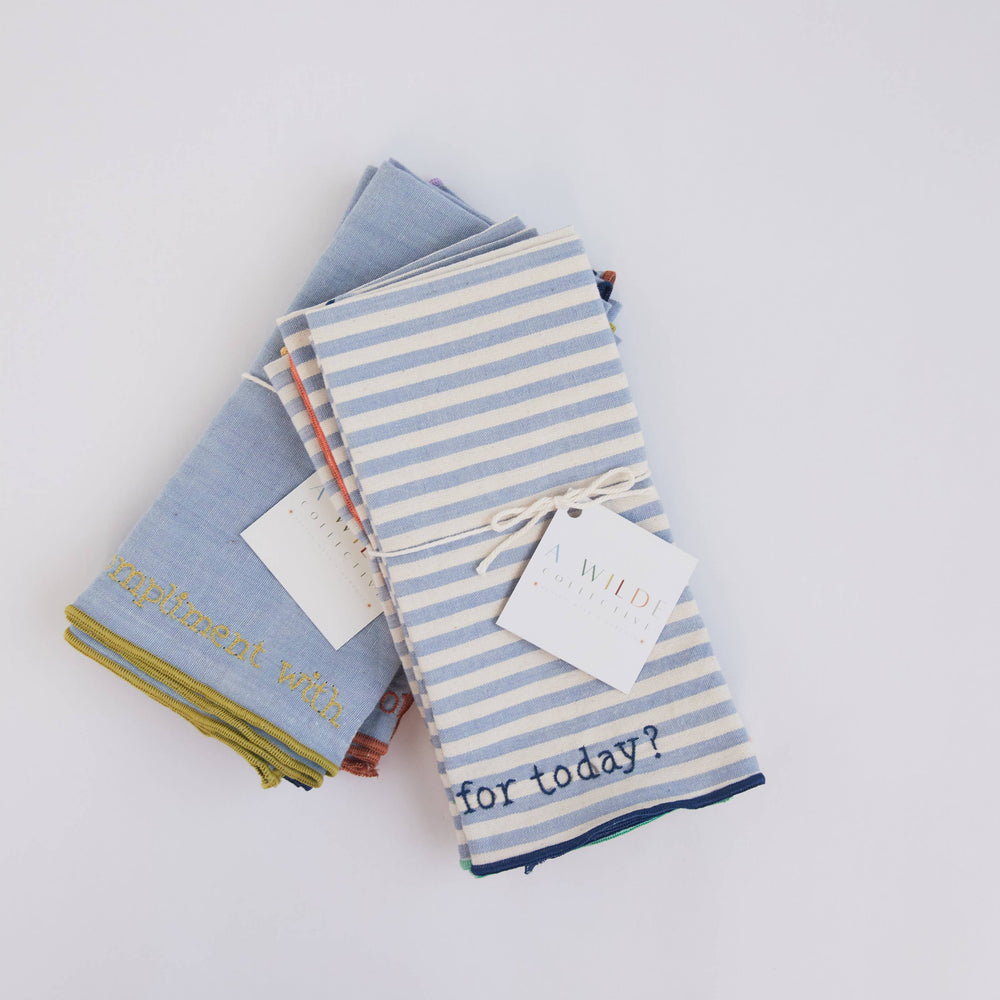 Flat lay of the Handwoven Conversation Dinner Napkins Classic Set with four unique embroidered prompts on natural chambray fabric