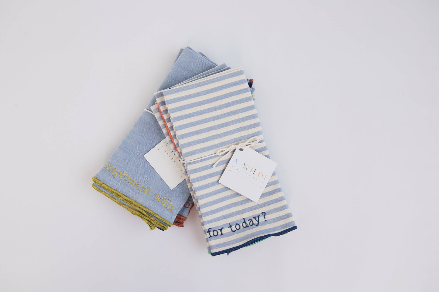 Flat lay of the Handwoven Conversation Dinner Napkins Classic Set with four unique embroidered prompts on natural chambray fabric
