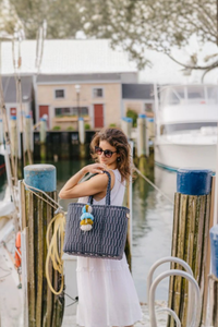 Navy Mesh Citron Tote with navy handles and colorful tassel, carried by a woman in a white dress near a marina.