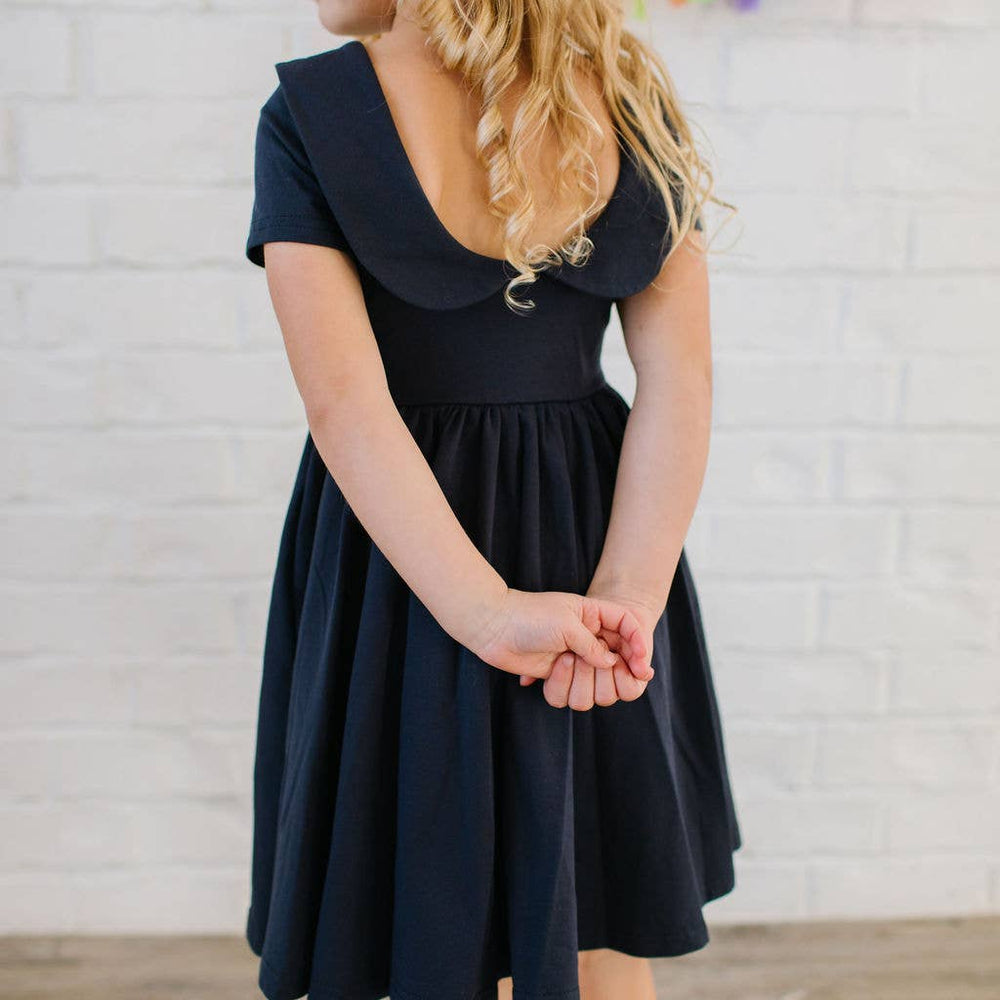 
                      
                        Toddler standing still in the Elizabeth Dress in navy, showing the scoop back and collar from behind.
                      
                    