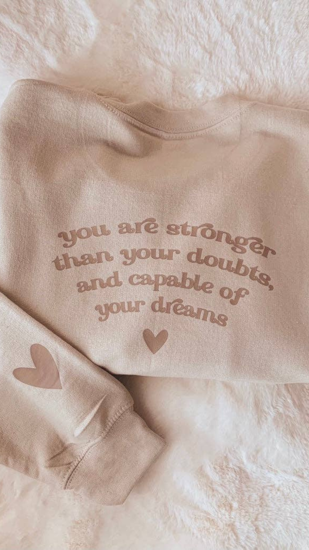 Neutral sand-colored sweatshirt with the inspirational message “You are stronger than your doubts, and capable of your dreams,” laid flat for full design view.