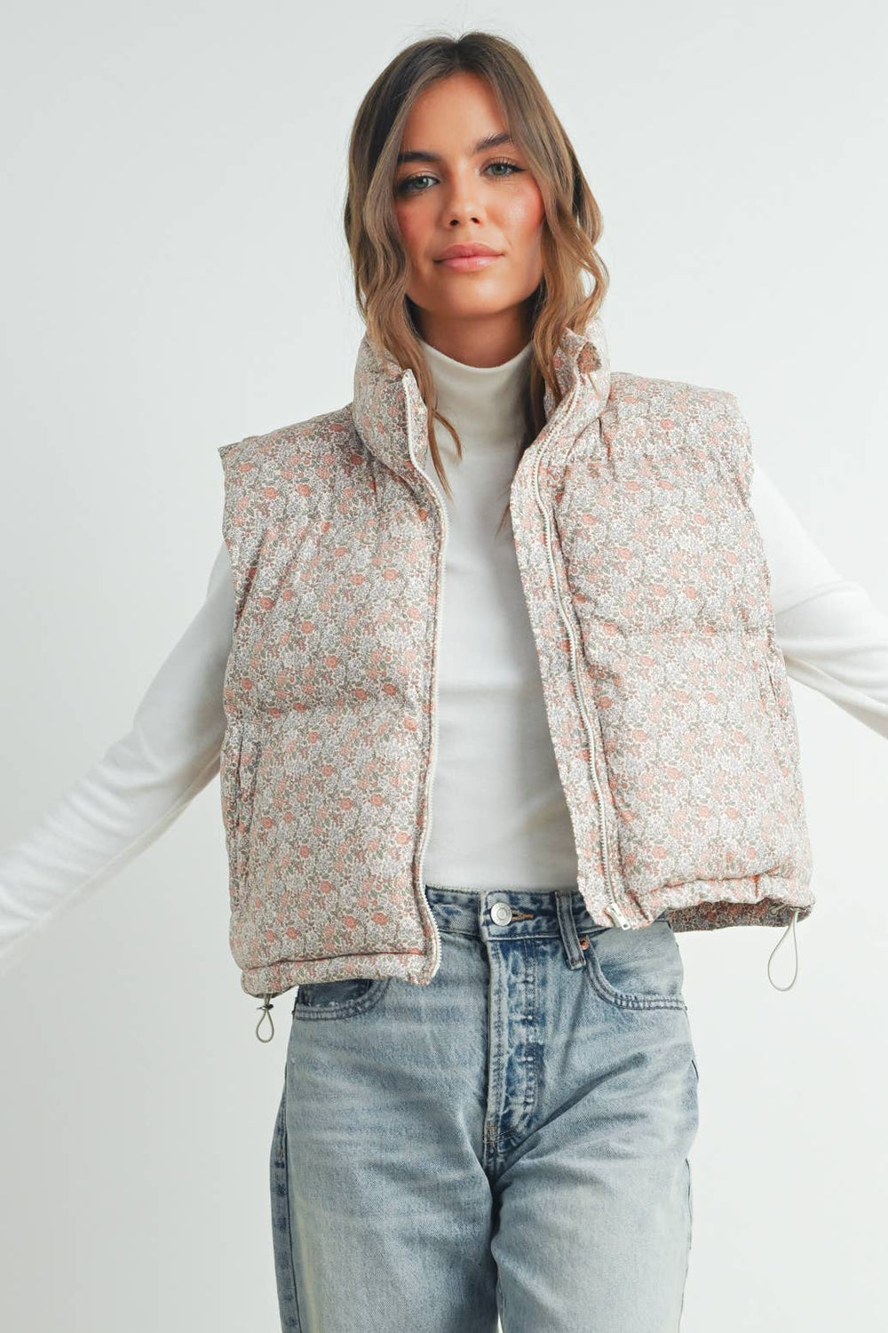 Model wearing the Floral High Neck Puffer Vest layered over a cream sweater, showing front snap closure and floral pattern