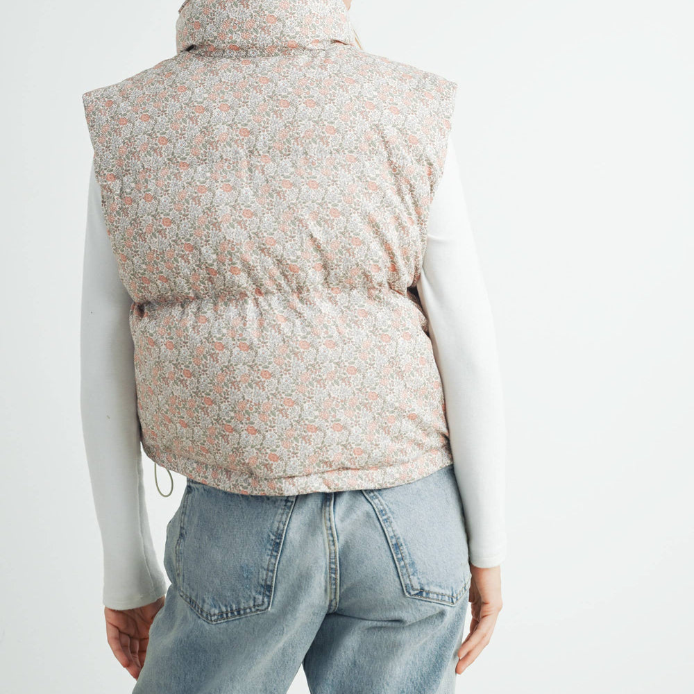 
                      
                        Back view of the Floral High Neck Puffer Vest on model paired with jeans, showcasing full floral pattern and structure of the vest
                      
                    