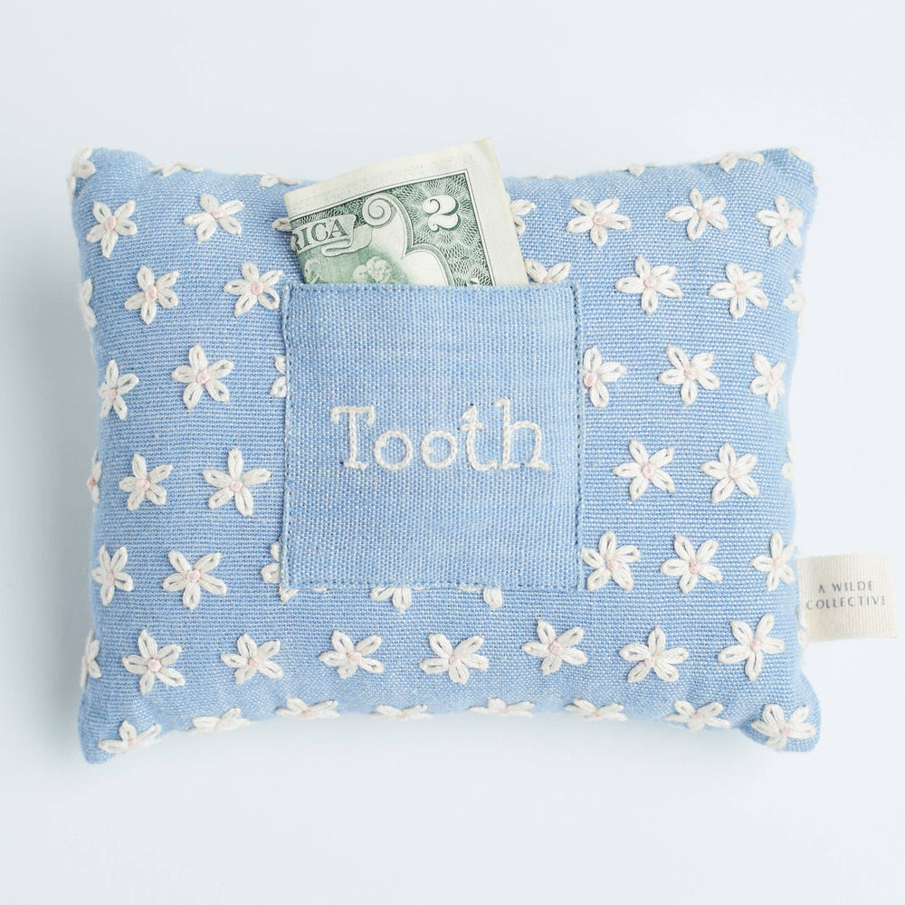 Handwoven floral tooth fairy pillow resting on a child’s bed, with a money tucked inside the front pocket