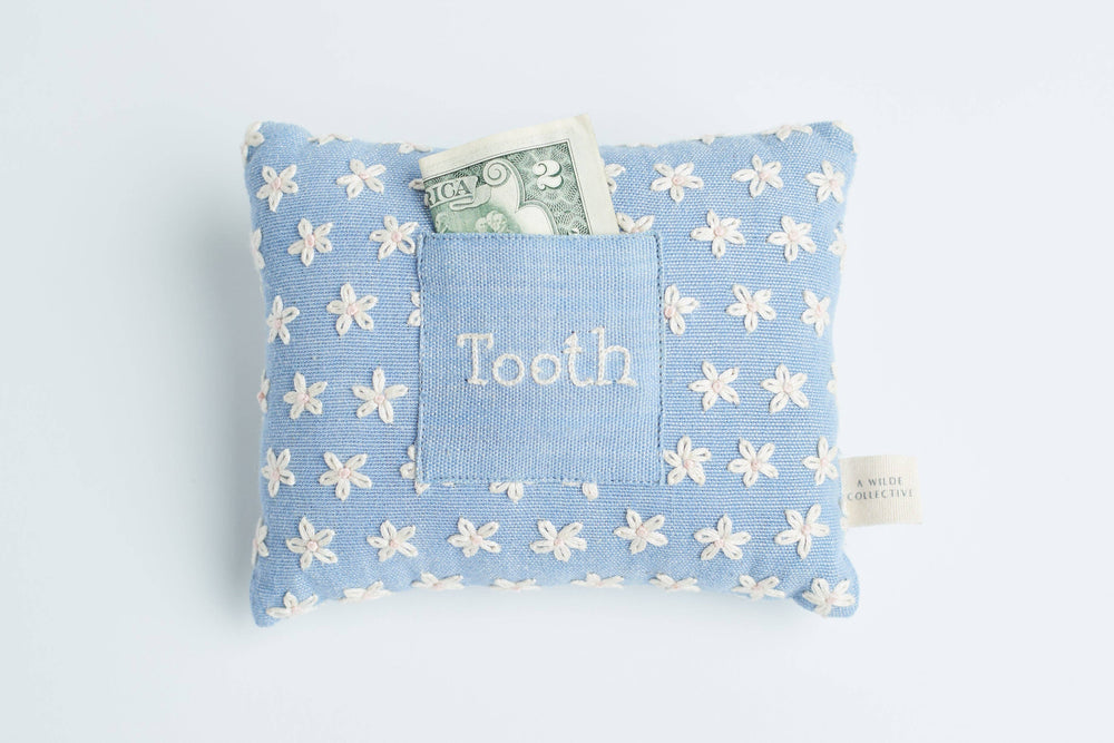 Handwoven floral tooth fairy pillow resting on a child’s bed, with a money tucked inside the front pocket