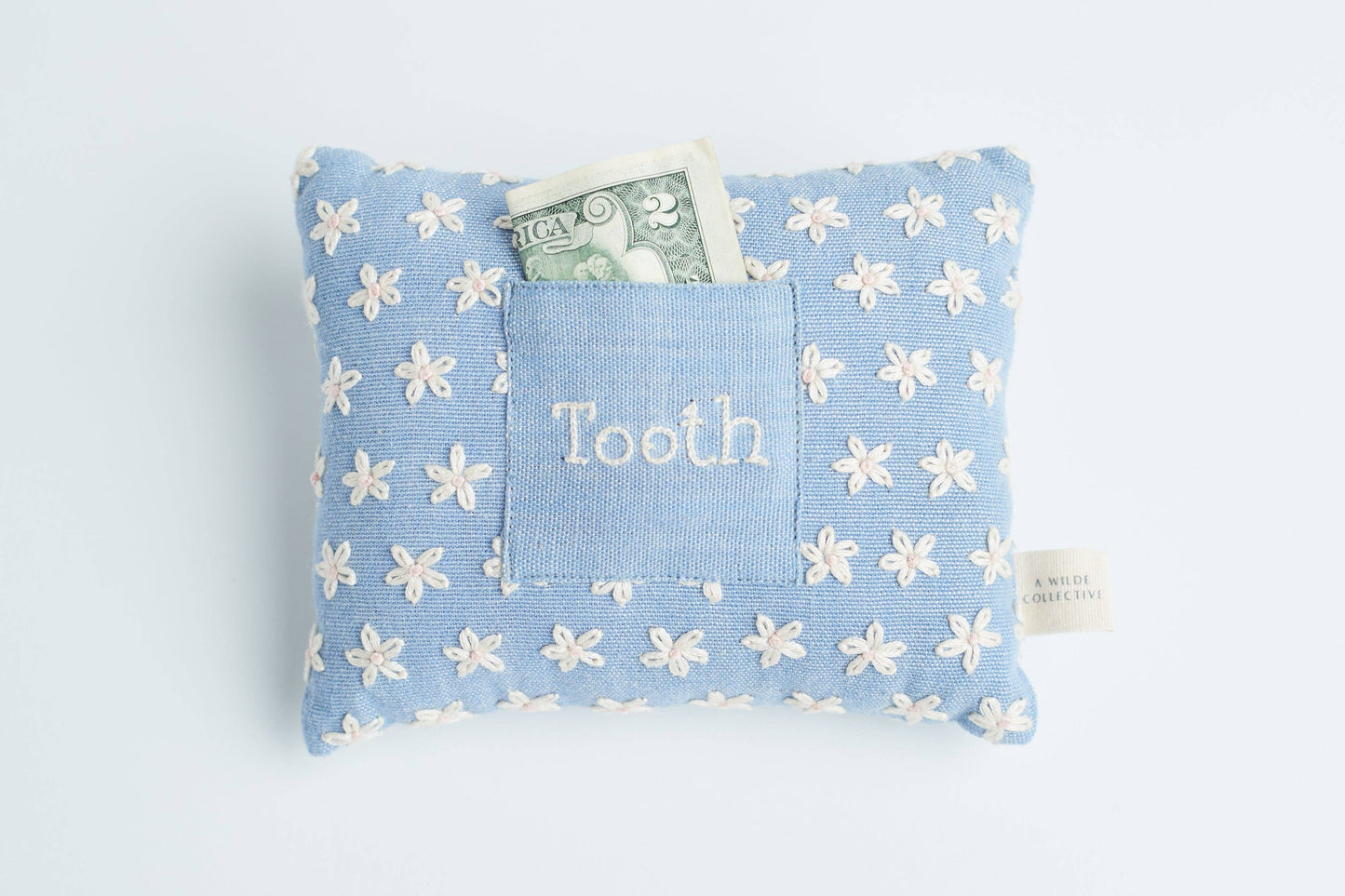 Handwoven floral tooth fairy pillow resting on a child’s bed, with a money tucked inside the front pocket