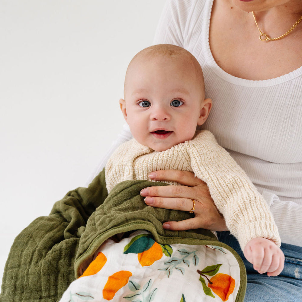 Baby wrapped in Fresh Clementine Quilt on mom’s lap, highlighting cozy, breathable muslin for comfort and warmth.