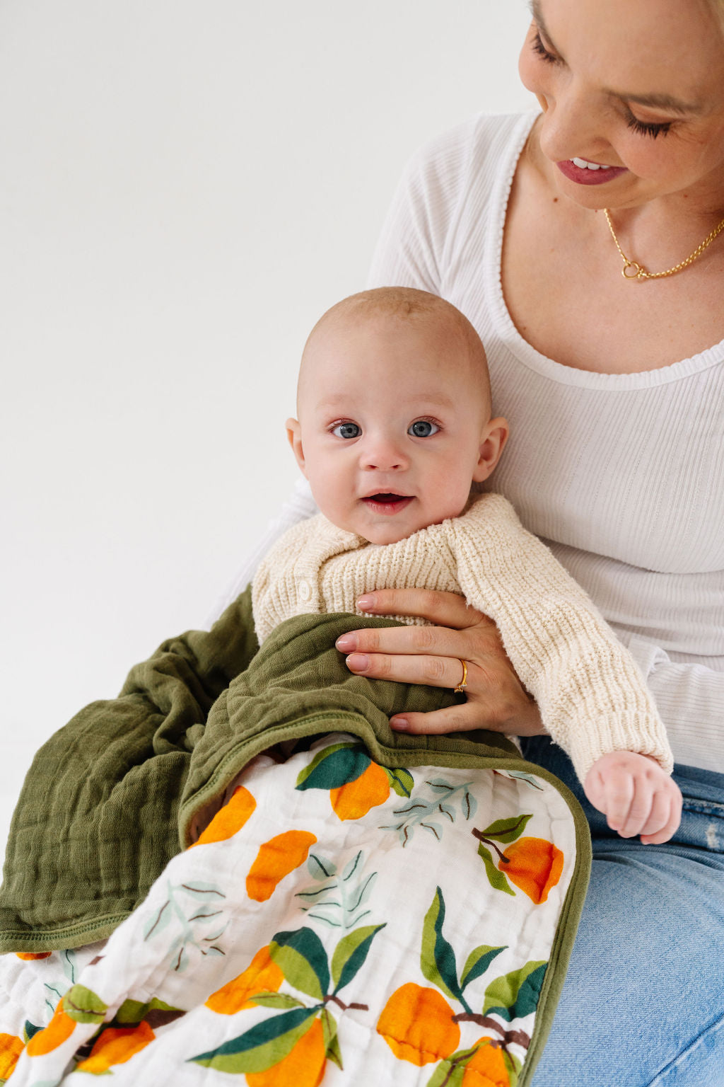 Baby wrapped in Fresh Clementine Quilt on mom’s lap, highlighting cozy, breathable muslin for comfort and warmth.