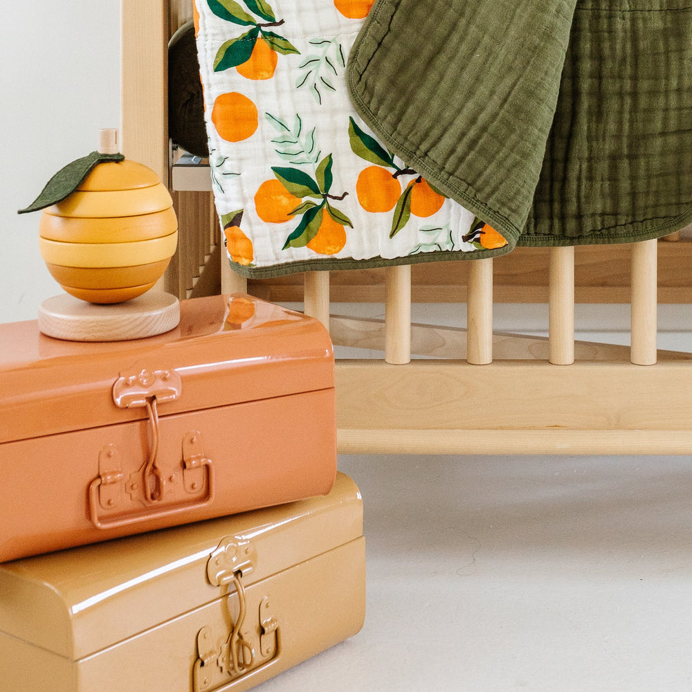 
                      
                        Fresh Clementine Quilt draped over side of crib, displaying soft texture and stylish design for baby’s nursery.
                      
                    