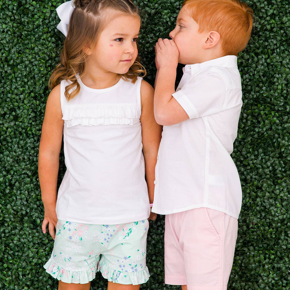 Girl in mint meadow floral ruffle shorts standing with boy in matching aqua stripe outfit, perfect sibling look for spring photos