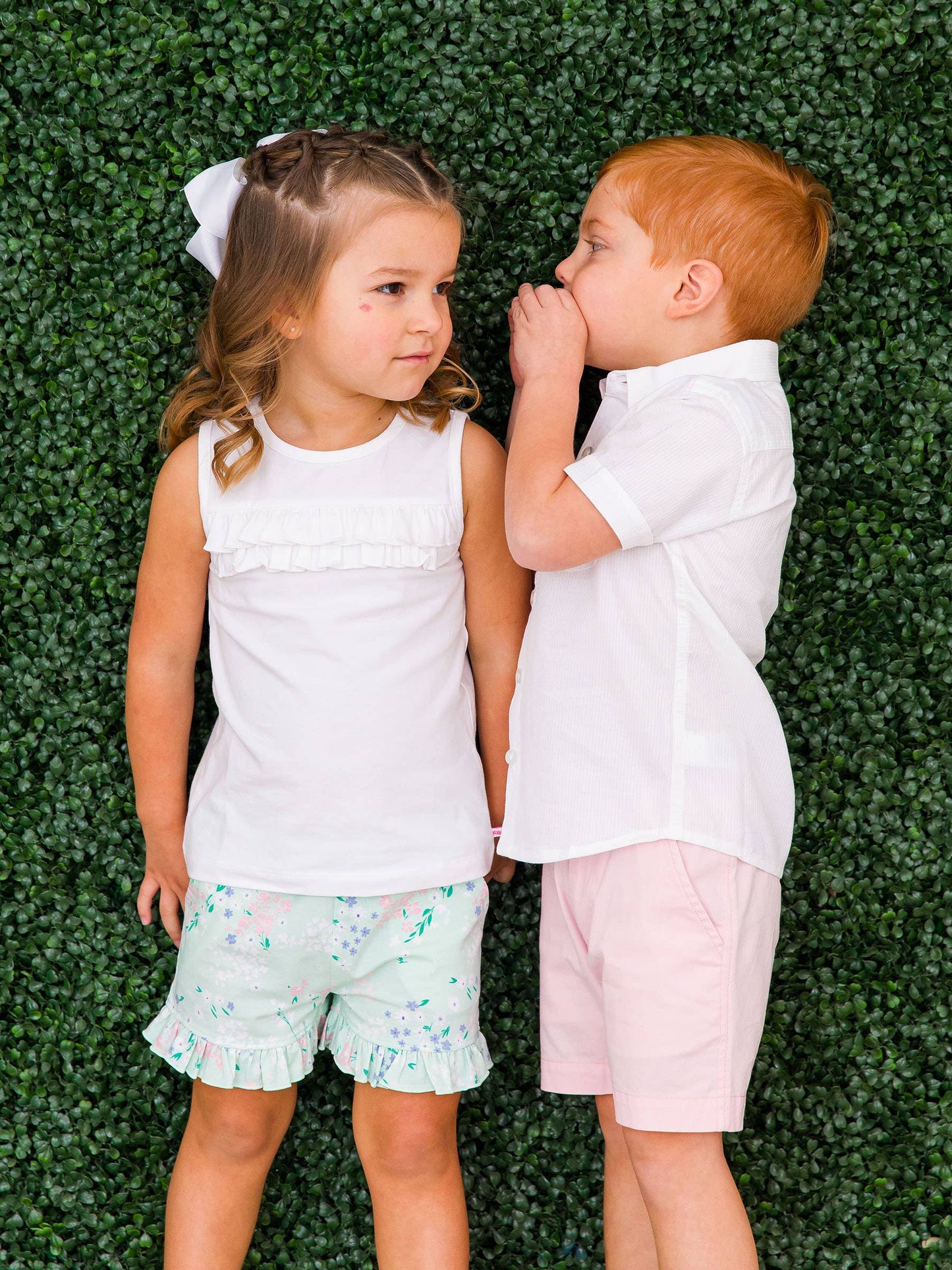 Girl in mint meadow floral ruffle shorts standing with boy in matching aqua stripe outfit, perfect sibling look for spring photos