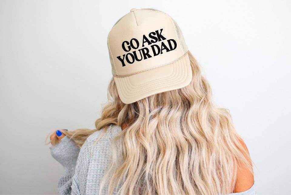 Beige trucker hat with Go Ask Your Dad embroidered in black, worn by a woman with long, wavy blonde hair.