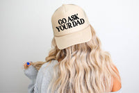 Beige trucker hat with Go Ask Your Dad embroidered in black, worn by a woman with long, wavy blonde hair.
