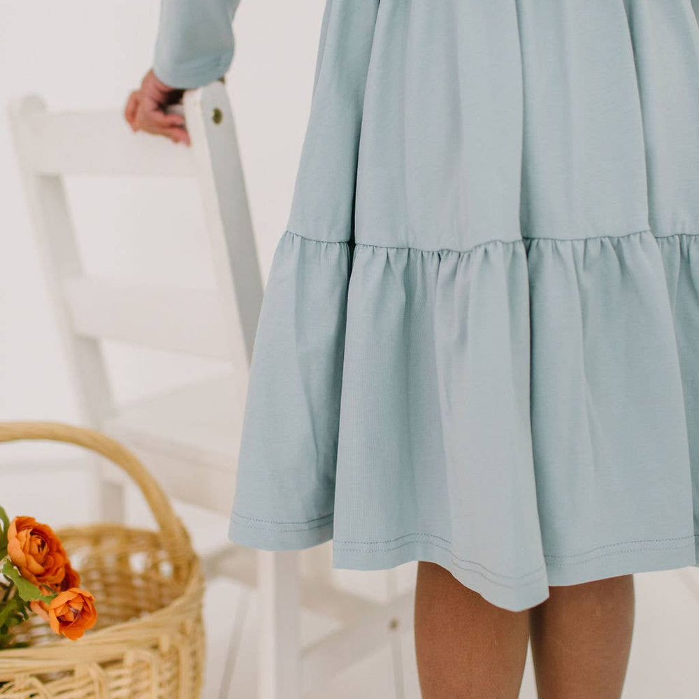 
                      
                        Close-up of the Gwendolyn Ruffle Dress in dusty blue, highlighting the soft fabric and midline ruffle details of the skirt.
                      
                    