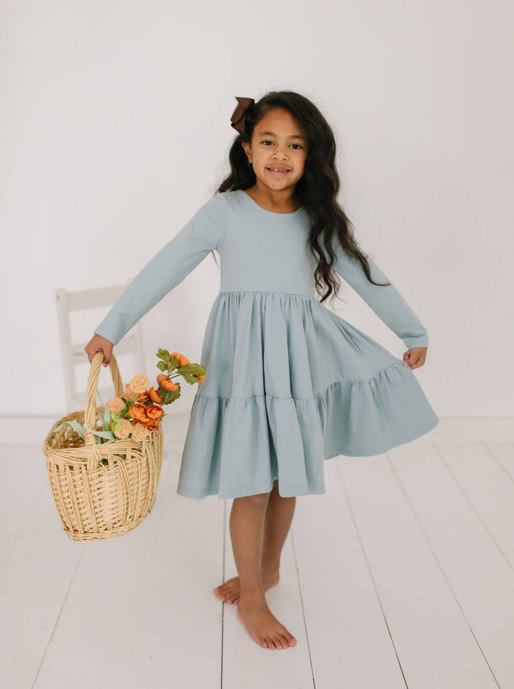 Toddler model holding out the skirt of the Gwendolyn Ruffle Dress in dusty blue to show its full twirl-ready design.