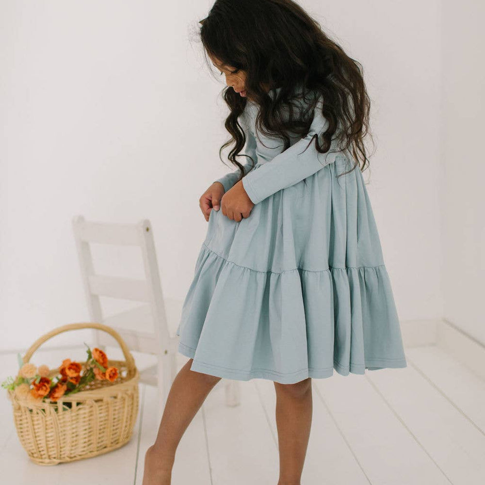 
                      
                        Toddler model showing the hidden pockets of the Gwendolyn Ruffle Dress in dusty blue, perfect for little treasures.
                      
                    