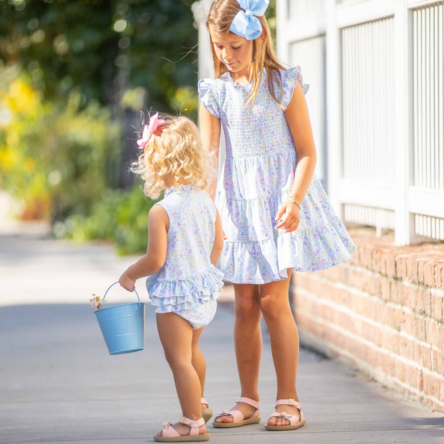 Back view of baby wearing the Kiawah Ruffle Bubble next to an older girl in the coordinating Kiawah dress—perfect for sibling photos and special occasions.