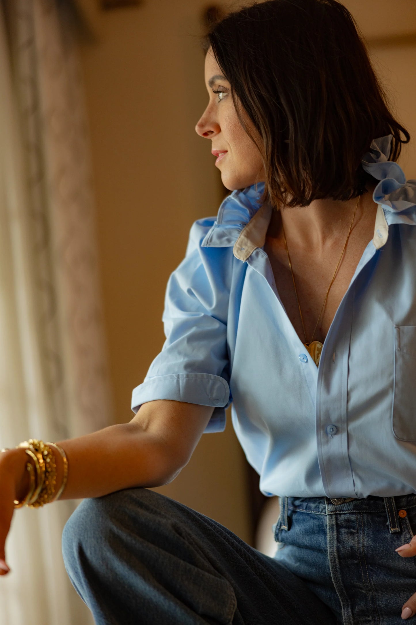 Designer Kate wearing KMJ Bonita light blue shirt with ruffle collar styled with casual shorts in a bright, peaceful hotel room in California.