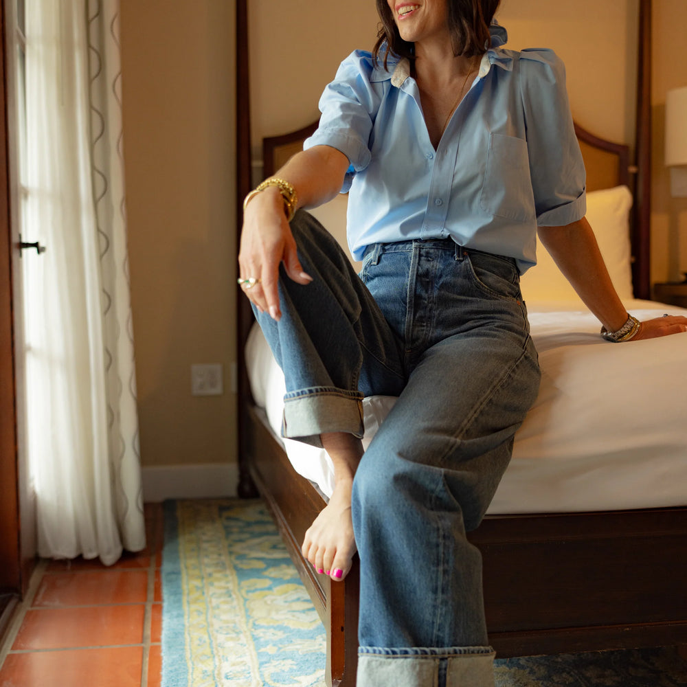 KMJ Bonita shirt in light blue with ruffle collar paired with casual shorts, styled by designer Kate in a serene hotel room setting in California.